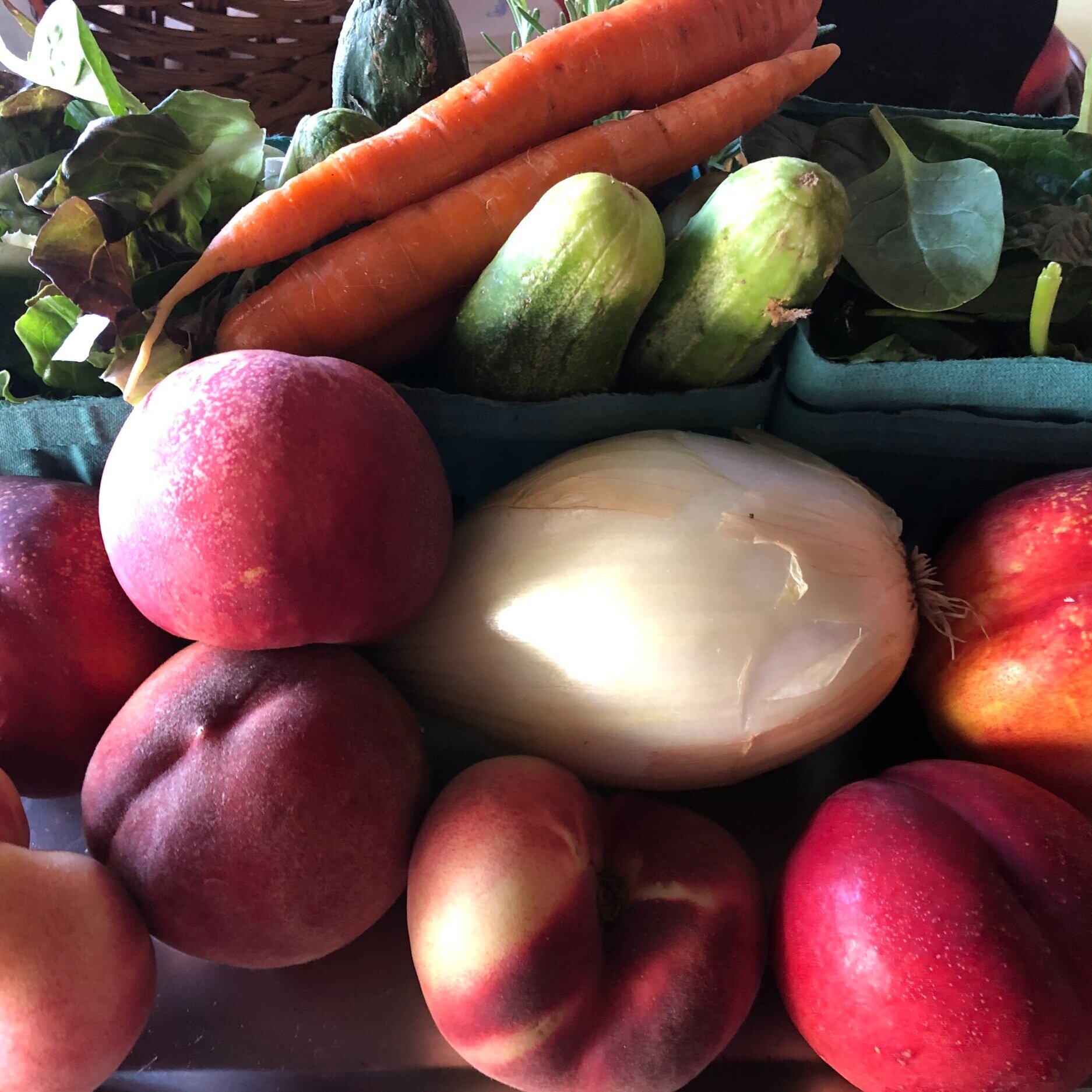 Colorful assortment of fresh fruits and vegetables, including peaches, apples, cucumbers, carrots, and a white onion, arranged attractively in baskets. Ideal for promoting healthy eating and farm-to-table cuisine.